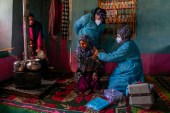 Kashmiri village girl Safia Banoo receives COVID vaccine as her family members warm themselves near a heater in Gagangir, northeast of Srinagar. [Dar Yasin/AP Photo]