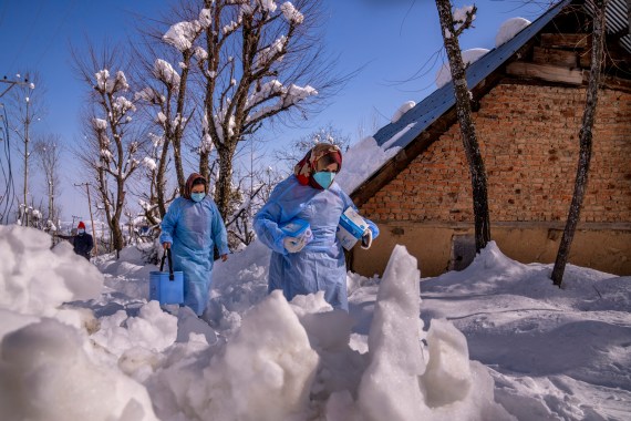 Healthcare workers, carry vaccines as they walk on a snow covered road during a COVID-19 vaccination in Indian controlled Kashmir