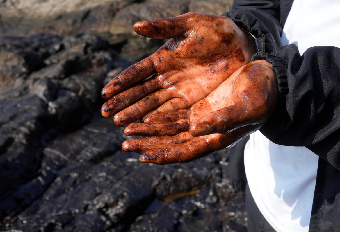 A cyclist shows his oil-covered hands after stopping to put them into the polluted water on Cavero beach in Ventanilla, Callao, Peru