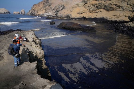 Workers look at the oil in the waters of Cavero Beach in Ventanilla, Callao, Peru
