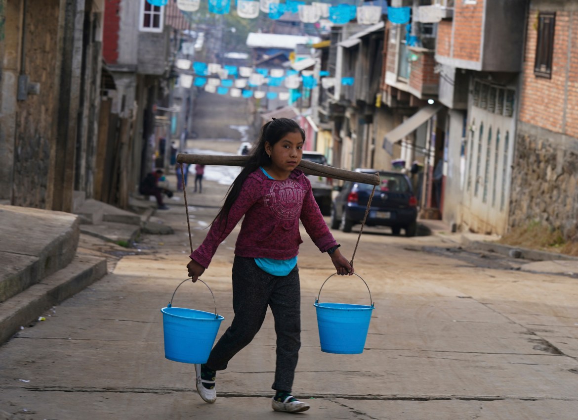 A girl hauling two buckets of water uses a carrying pole in the Puerpecha Indigenous community of Comachuen, Mexico