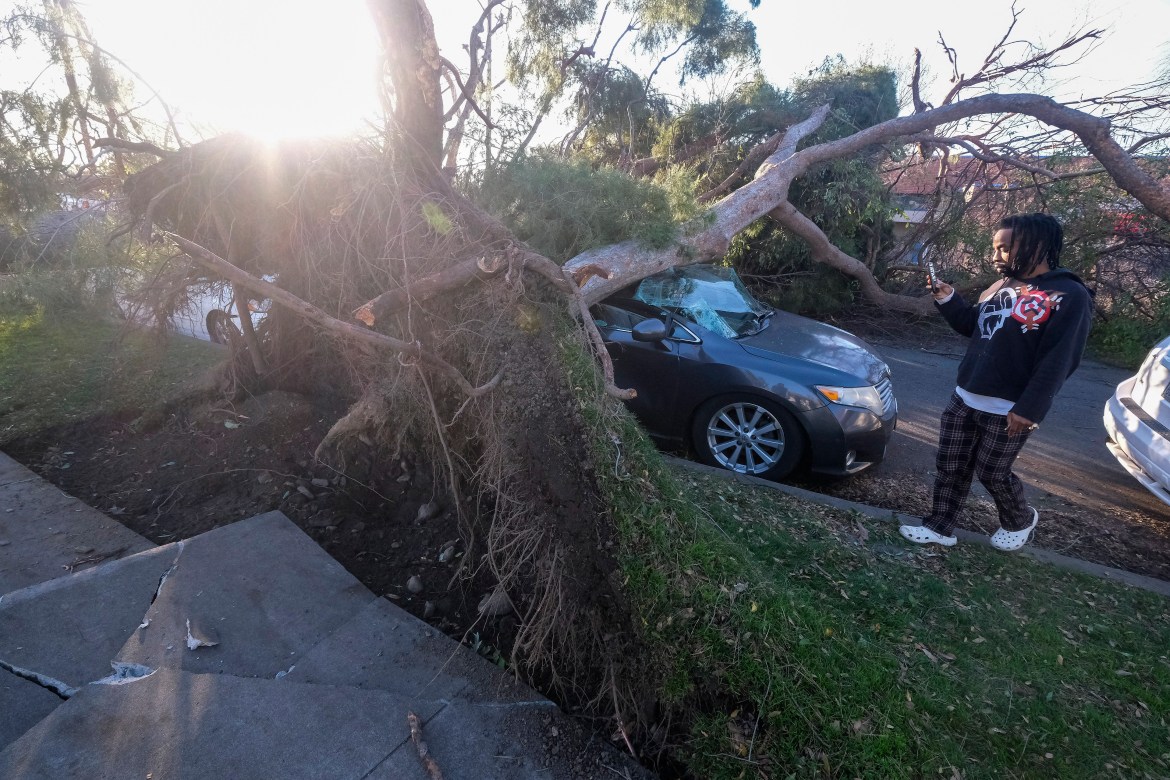Brandon Crenshaw takes photos as a fallen tree sits on top of his car after strong winds in Upland