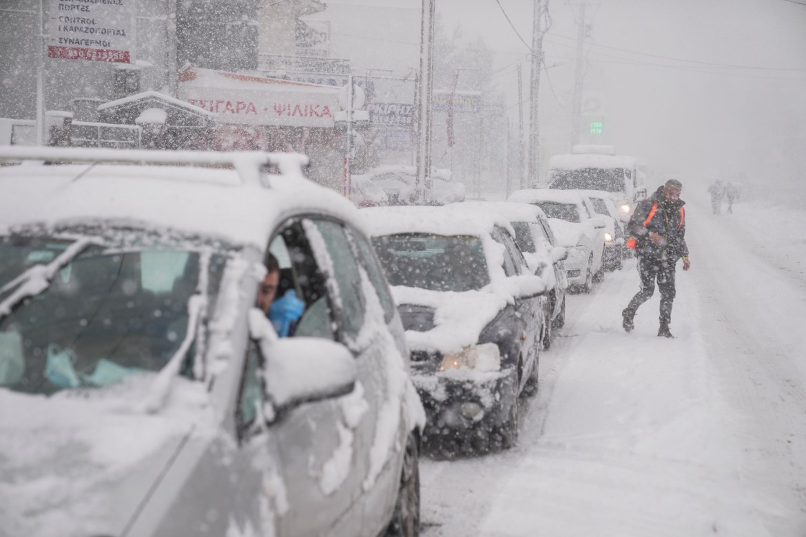 Vehicles drive as a man cross a street during snowfall in Agios Steganos, north of Athens