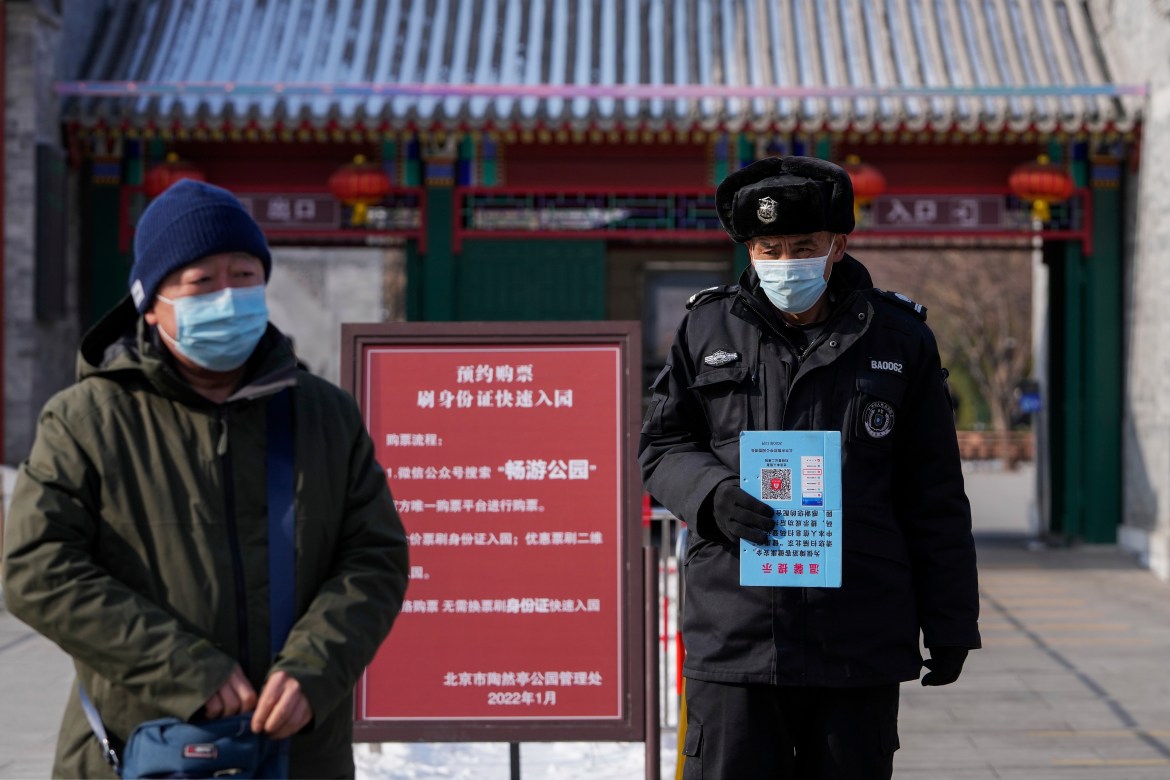 A man wearing a face mask to help protect from the coronavirus walks by a security guard holding a health code notice at an entrance gate to a park in Beijing, Tuesday, Jan. 25, 2022. Hong Kong has already suspended many overseas flights and requires arrivals be quarantined, similar to mainland China's "zero-tolerance" approach to the virus that has placed millions under lockdowns and mandates mask wearing, rigorous case tracing and mass testing. (AP Photo/Andy Wong)