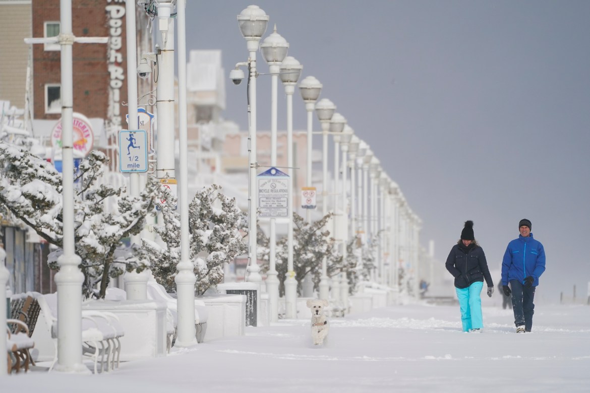 A dog is followed by a couple as the stroll on the snow-covered boardwalk, Saturday, Jan. 29, 2022, in Ocean City,Maryland