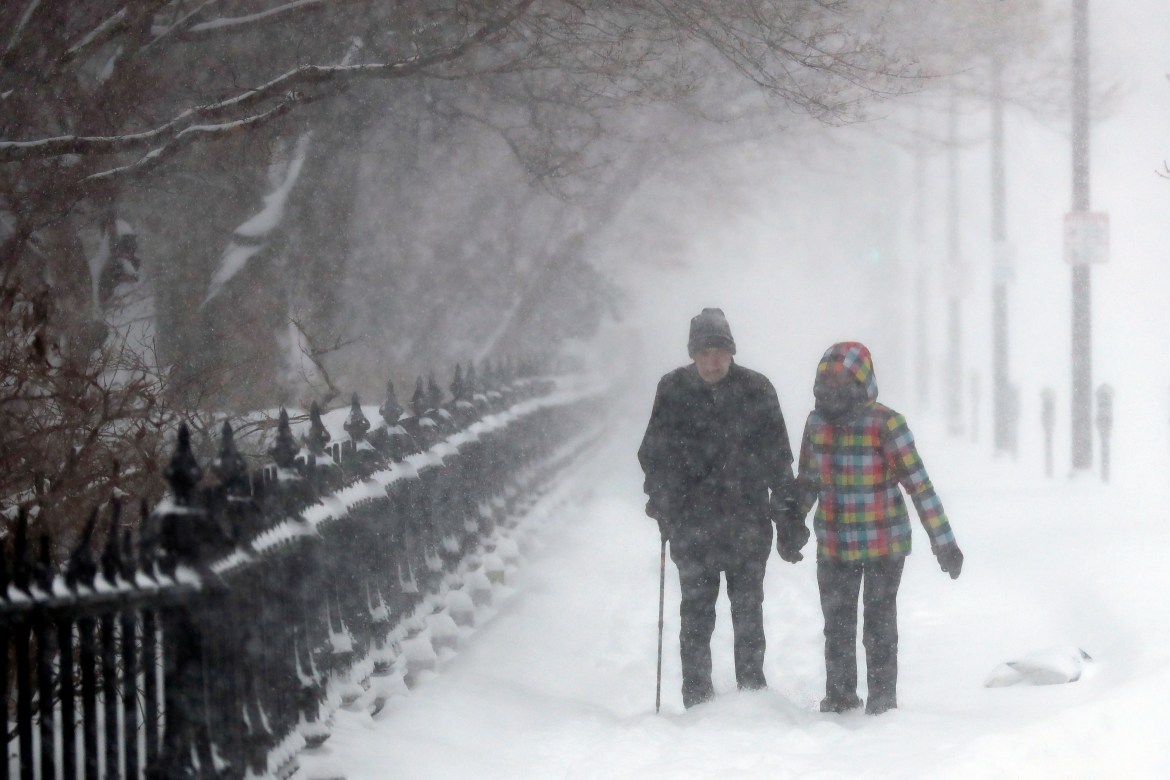 A couple walks through snow on Beacon Street past the Public Garden, Saturday, Jan. 29, 2022, in Boston