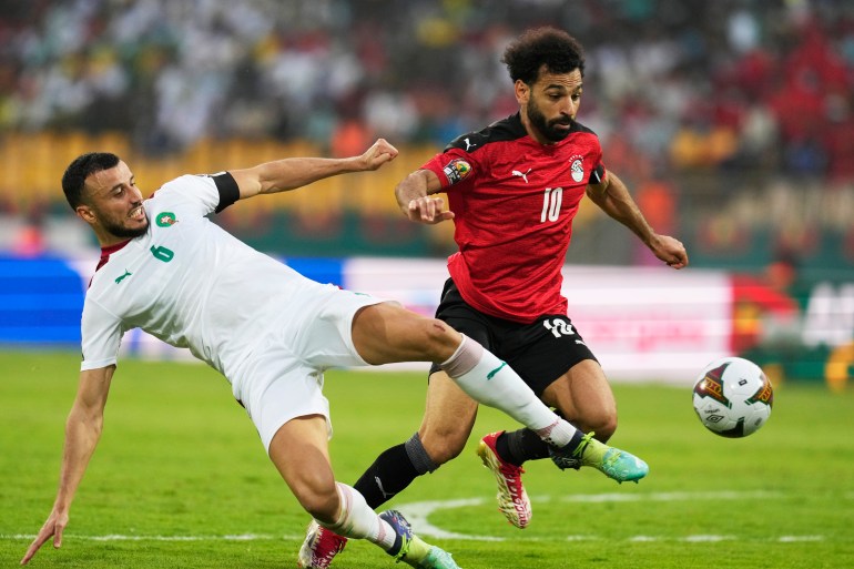 Morocco's captain Romain Saiss, left, falls as he fails to defend against Egypt's Mohamed Salah during the African Cup of Nations 2022 quarter-final soccer match between Egypt and Morocco at the Ahmadou Ahidjo stadium in Yaounde, Cameroon, Sunday, Jan. 30, 2022. (AP Photo/Themba Hadebe)