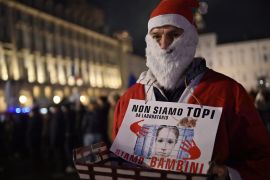 A man dressed as Santa Claus holds a sign that reads "We are not mice, we are children" in a town square in Turin, Italy