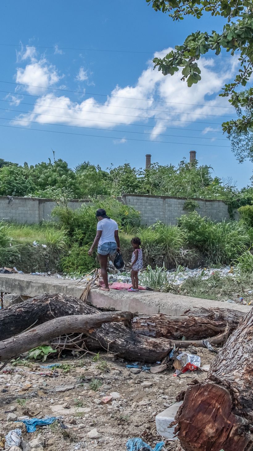 A woman and girl cross a bridge surrounded by trash