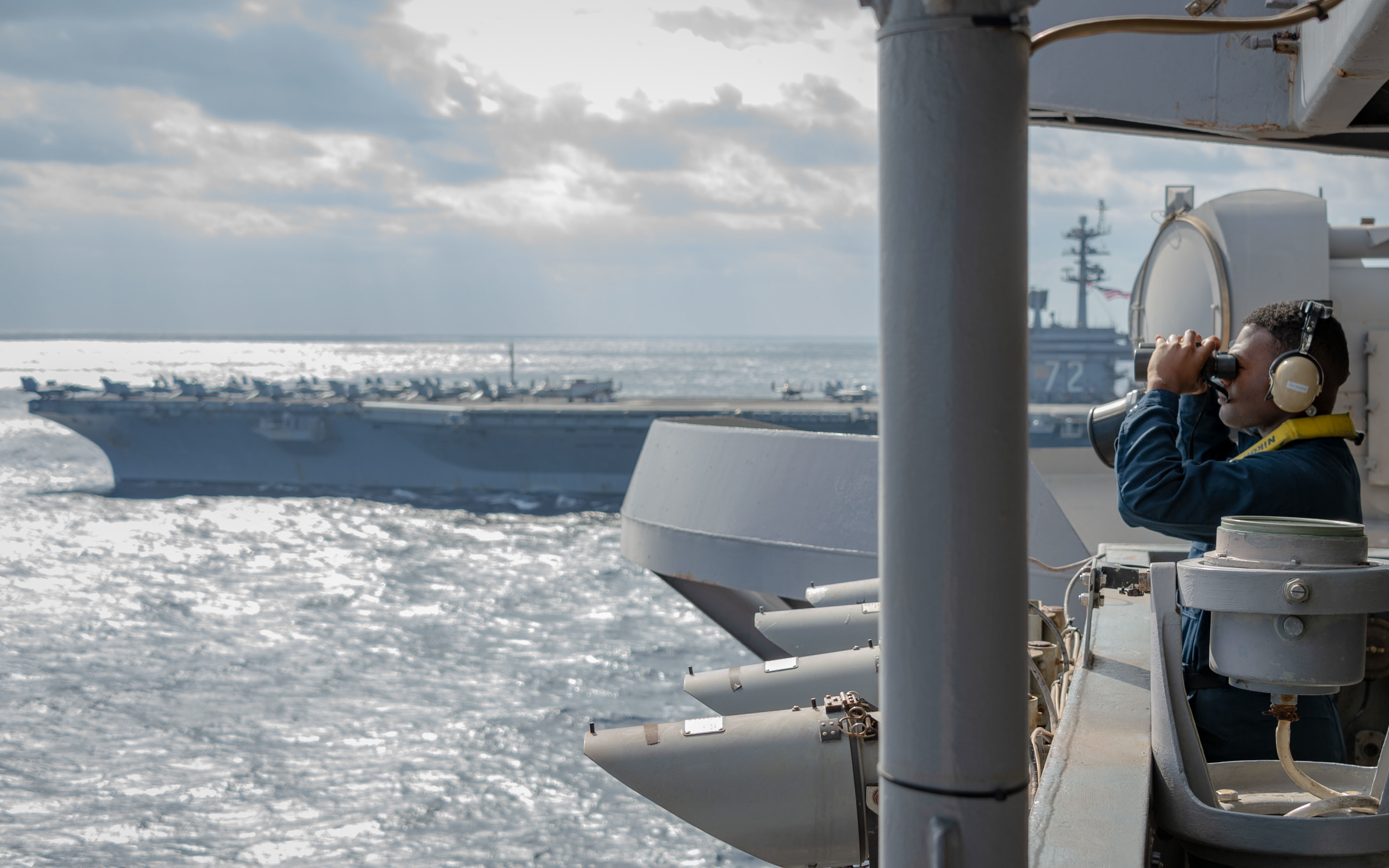 Un marinaio sul ponte della USS Carl Vinson osserva attraverso il binocolo durante le esercitazioni nel Mar Cinese Meridionale