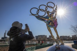 A woman in China takes a photo of a sculpture of figure skaters and the Olympic rings against the sun
