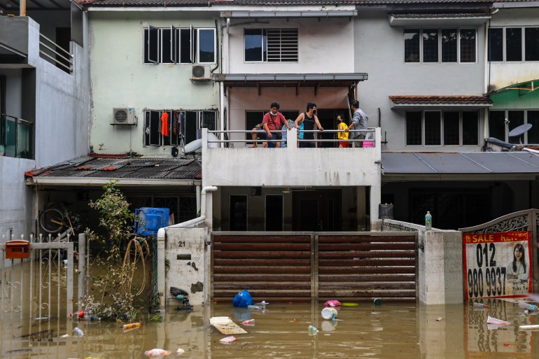 A family stand on the first floor balcony of their three storey terraced house looking at the browm flood waters that have inundated the street and flooded their home
