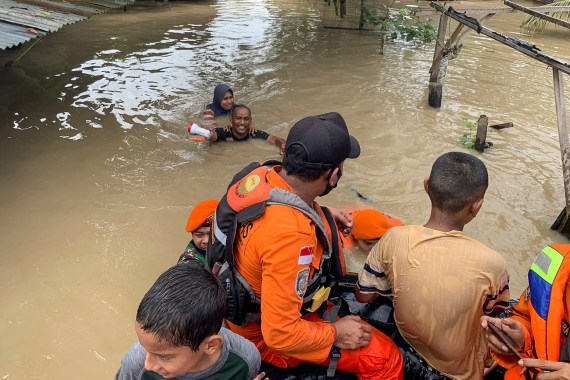 A rescuer in Indonesia's Aceh brings a woman to safety by wading through shoulder deep milky brown water after serious flooding hit the area