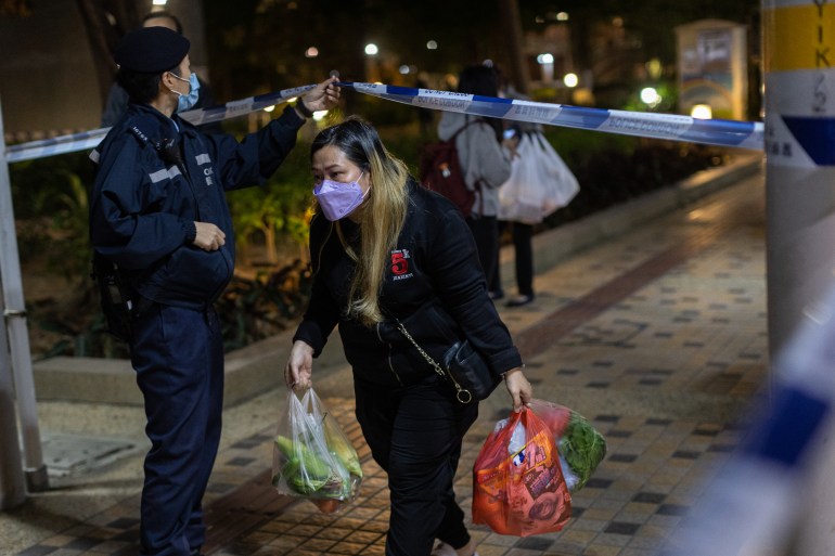 A female resident carries three plastic bags of groceries into a government housing complex beneath a police tape and watching officer