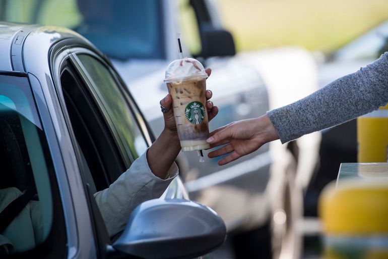 An employee passes a drink order to a customer at the drive-thru of a Starbucks Corp. coffee shop in Rodeo, California