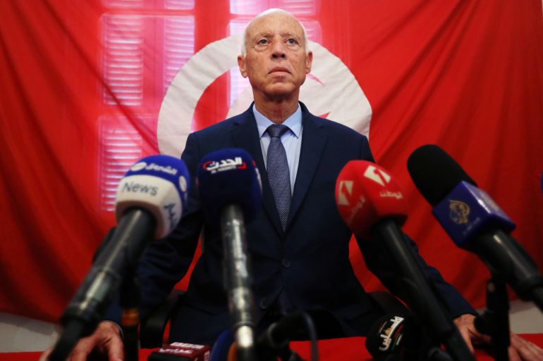 President Kais Saied stands in front of the Tunisian flag.