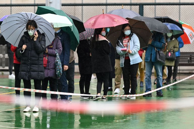 Poepel in Hong Kong queue beneath umbrellas in the rain to get tested for COVID-19
