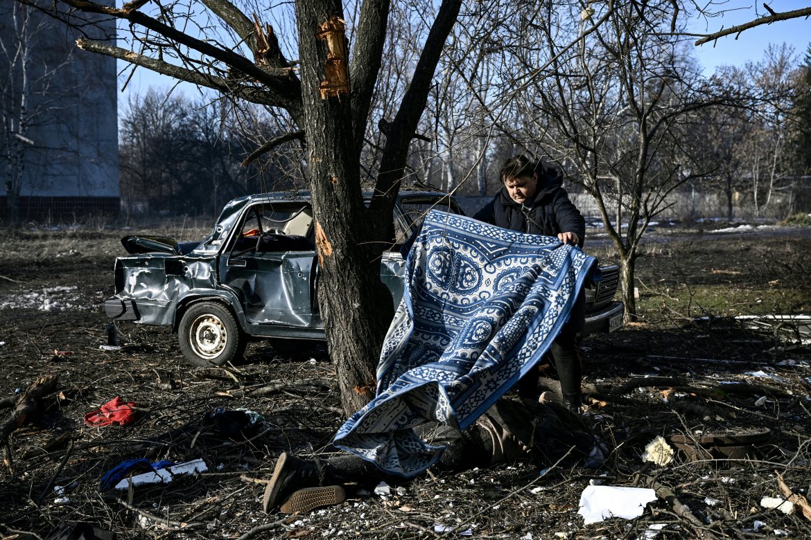 A man uses a carpet to cover a body stretched out on the ground after bombings on the eastern Ukraine town of Chuguiv