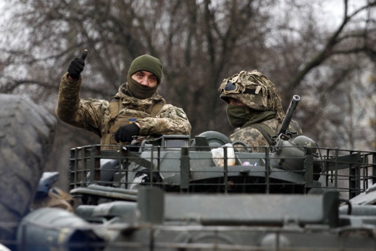A Ukrainian serviceman gives a thumbs-up sign riding atop a military vehicle