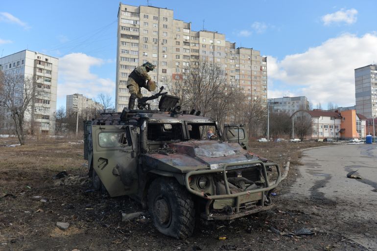 A Ukrainian Territorial Defence fighter examines a destroyed Russian infantry mobility vehicle GAZ Tigr after the fight in Kharkiv [Sergey Bobok/AFP]