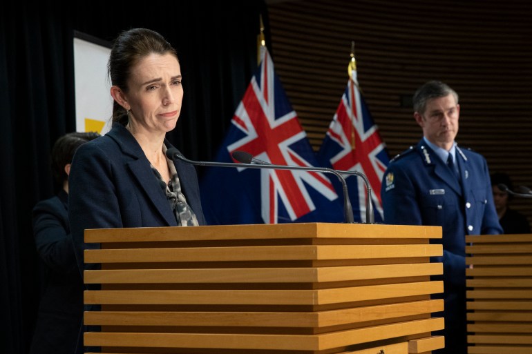 New Zealand Prime Minister Jacinda Ardern speaking to the media from a lectern with New Zealand flags behind 