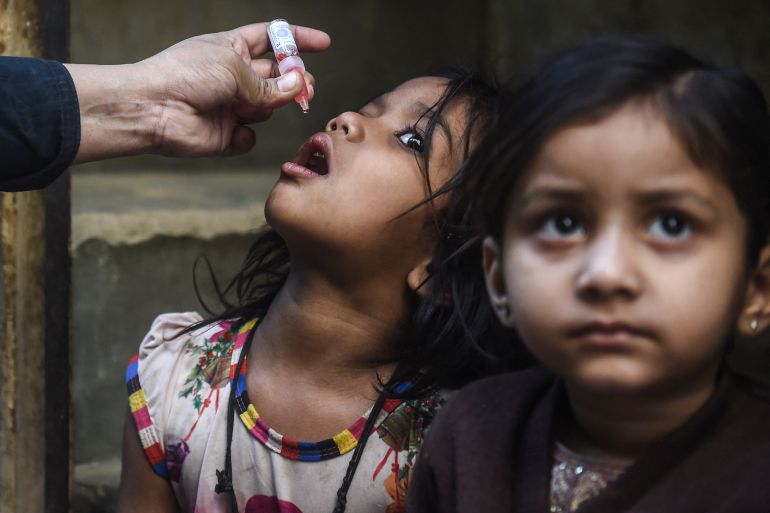 A young girl in Karachi is given drops of polio vaccine on her tongue while a friend sits by