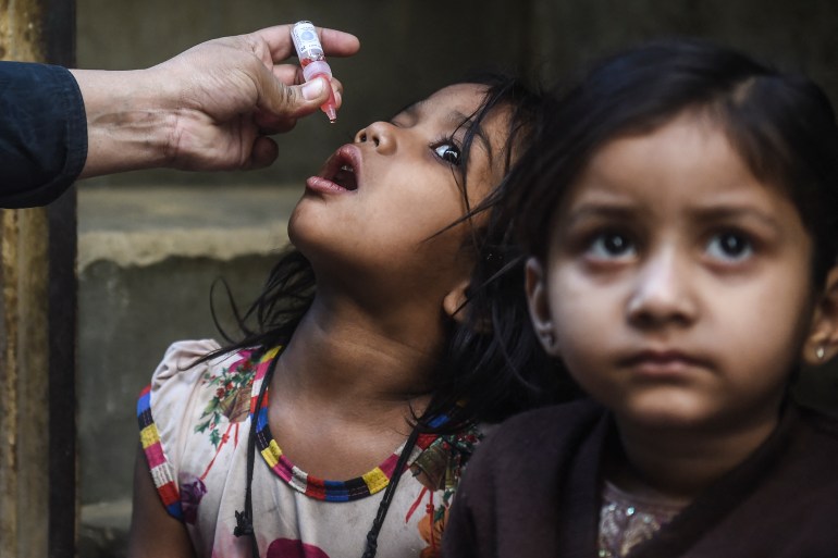 A young girl in Karachi is given drops of polio vaccine on her tongue while friend sits by