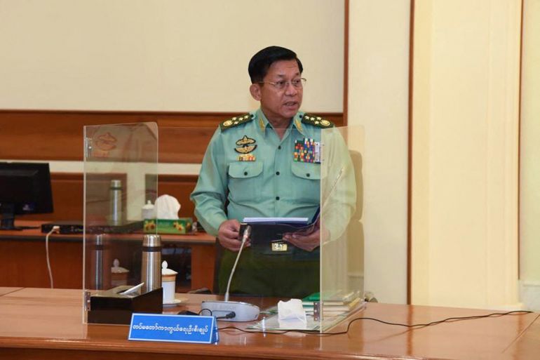 Myanmar coup leader Min Aung Hlaing in pale green military shirt with insignia and epaulettes stands at a desk in the capital Naypyidaw