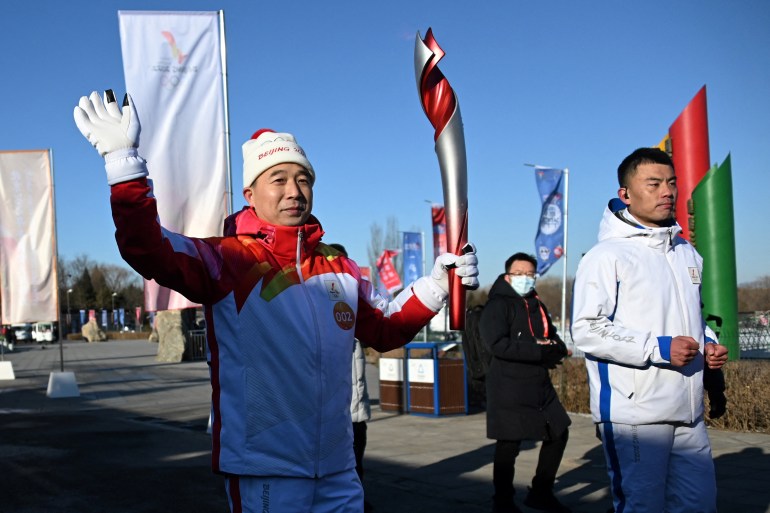 Chinese astronaut Jing Haipeng running with the Olympic Torch and waves against a blue sky in Beijing