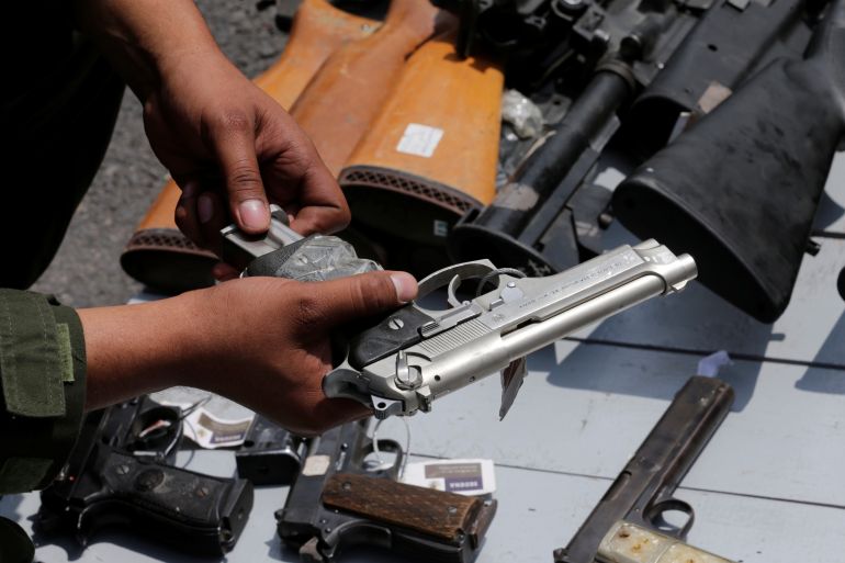 A Mexican soldier holds up a gun next to other weapons seized from alleged drug traffickers or handed in by residents before they are destroyed at a military zone in Mexico City,