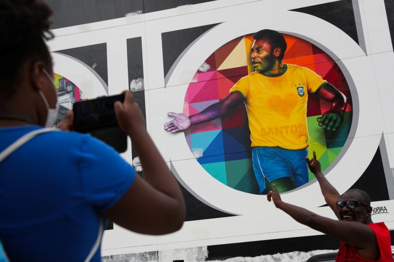 A person takes a picture of a mural depicting Pele