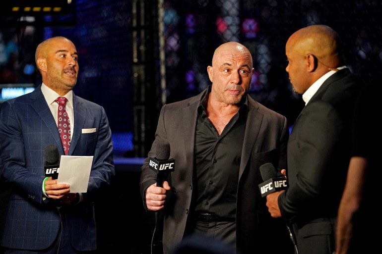 Joe Rogan (centre) is seen holding a UFC microphone along with two other presenters during UFC 261 at VyStar Veterans Memorial Arena