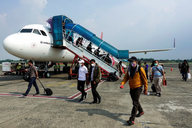Passengers wearing protective masks walk on the tarmac as they arrive at the Halim Perdanakusuma airport in Jakarta, Indonesia, October 20, 2021.