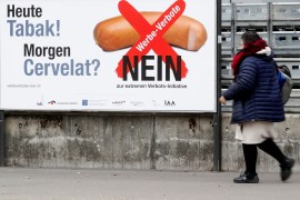 A woman walks past a poster reading "Today tobacco! Tomorrow cervelat sausage? Advertising ban