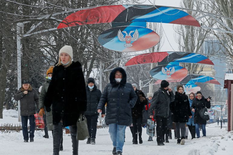 Pedestrians are seen walking under boards displaying the flag and coat of arms of the self-proclaimed Donetsk People's Republic
