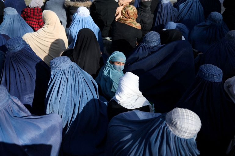 A girl sits in front of a bakery in the crowd with Afghan women waiting to receive bread in Kabul