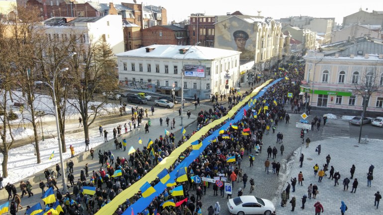 A crowd of protesters hold up a long Ukrainian flag as they march down a street in Kharkiv, Ukraine