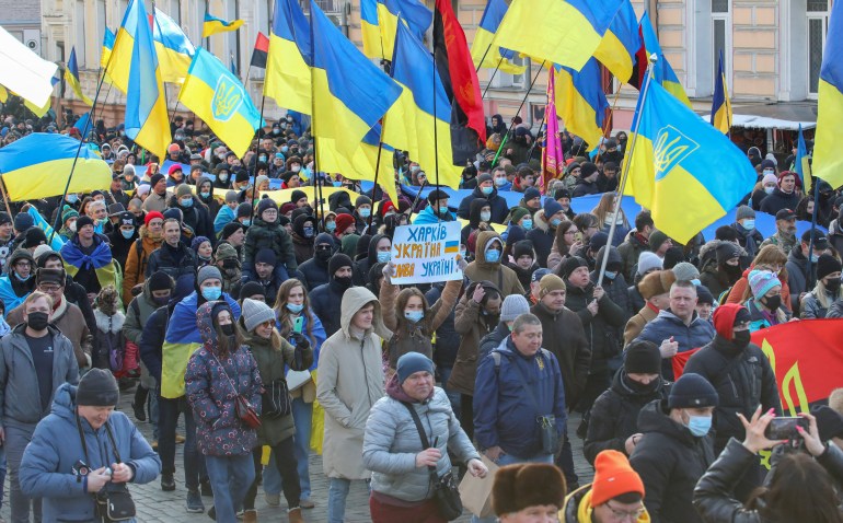 A crowd of demonstrators march down a street holding up Ukrainian flags in Kharkiv, Ukraine