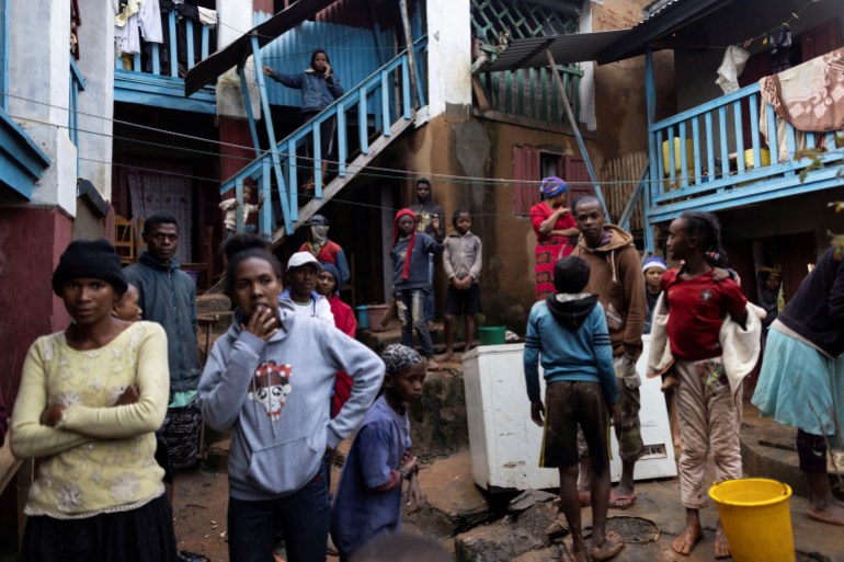 Men and women stand amid mud and water outside damaged homes after Cyclone Batsirai