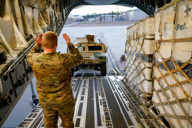 Military personnel with the 82nd Airborne Division load a HMMWV aboard a C-17 transport plane for deployment to Eastern Europe