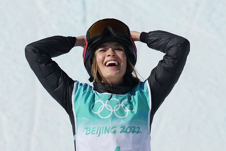 Eileen Gu, wearing a turquoise and white Beijing 2022 vest over a black sweater celebrates her victory in the freeski Big Air
