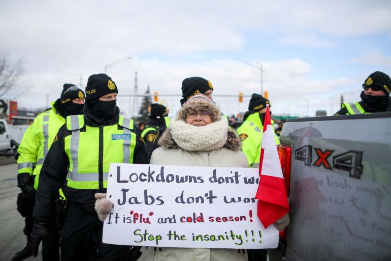 A protester stands in front of police officers, who stand guard on a street after Windsor Police said that they are starting to enforce a court order to clear truckers and supporters who have been protesting against coronavirus disease (COVID-19) vaccine mandates by blocking access to the Ambassador Bridge