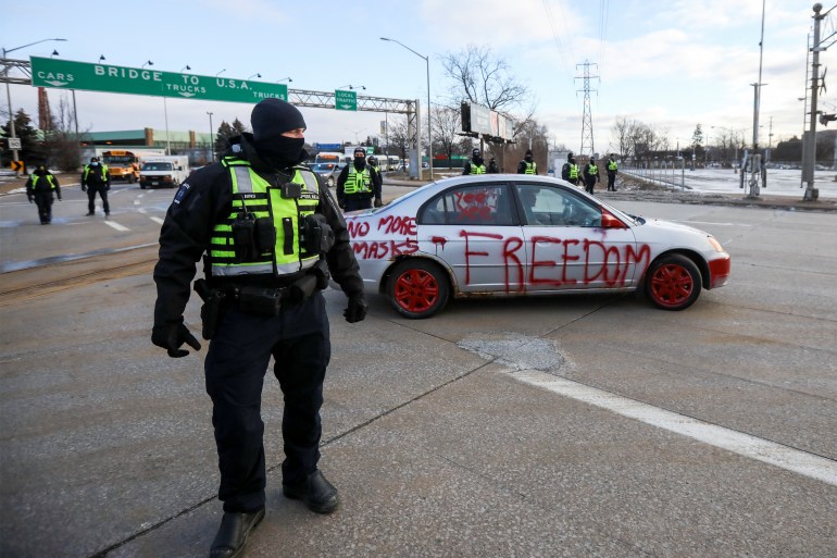 Police officers stand guard in front of a car during COVID-19 protests in Canada