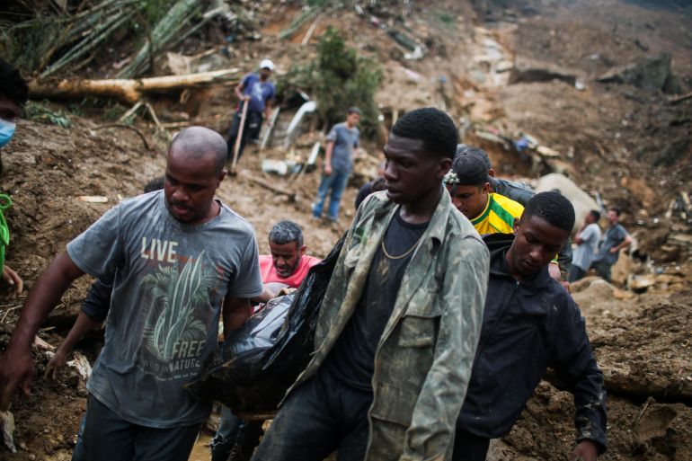 two men in mud covered clothes carry out a a victim of the landslides on a stretcher
