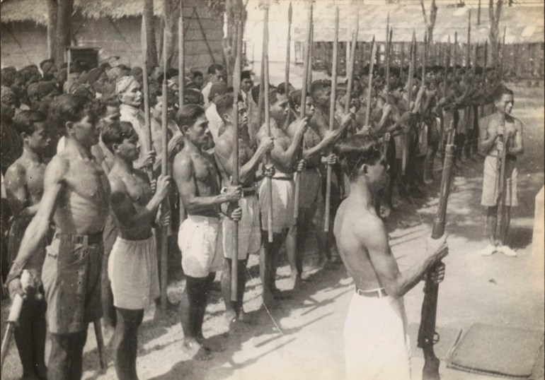 Young Indonesian men wearing short sarongs stand in formation with their spears during the war for independence against the Dutch