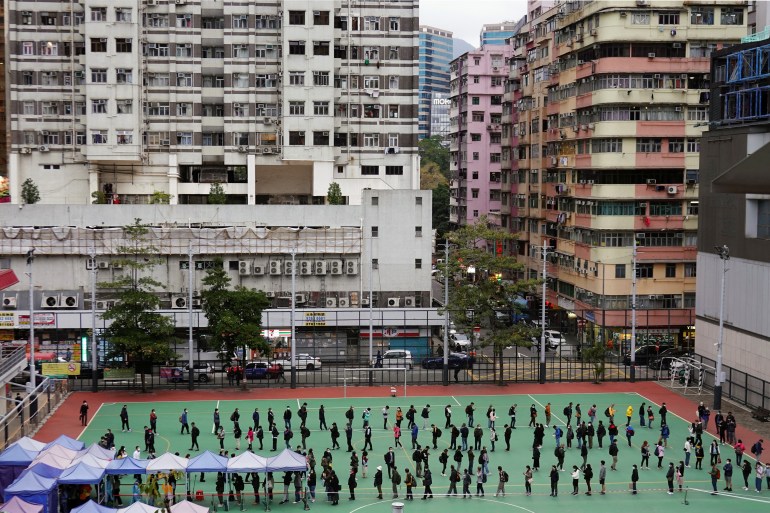 People queue on a sports field for COVID tests amid Hong Kong's densely-packed skyscrapers