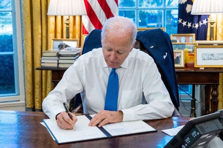 Biden signs an executive order in the White House against a backdrop of the US flag 