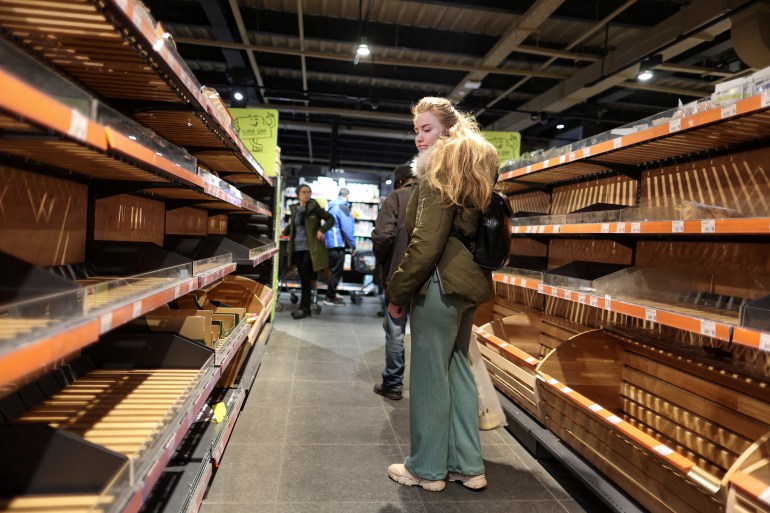 A woman is seen looking at empty shelves in a Kyiv shop
