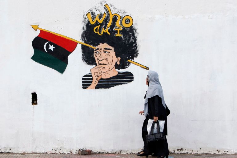 Two Libyan women walk past graffiti depicting Muammar Gaddafi
