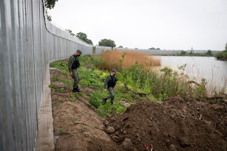 Greek policemen patrol alongside a steel wall at Evros river
